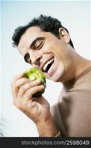 Low angle view of a mid adult man holding a green bell pepper and smiling