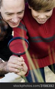 Low angle view of a mid adult man with his son holding a magnifying glass