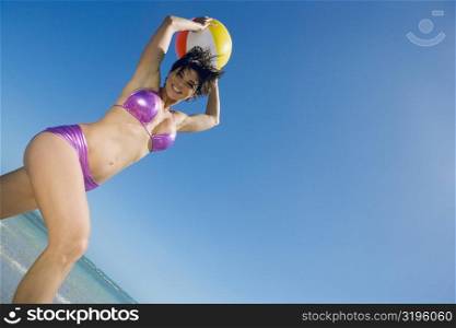 Low angle view of a mid adult woman playing with a beach ball on the beach