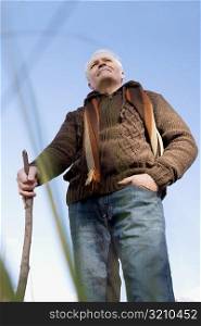 Low angle view of a senior man standing and holding a stick