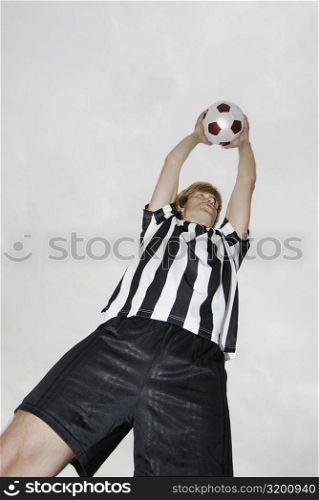 Low angle view of a soccer player holding a soccer ball over his head