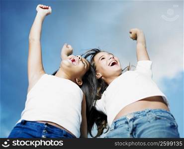 Low angle view of a teenage girl and her sister with their arms raised