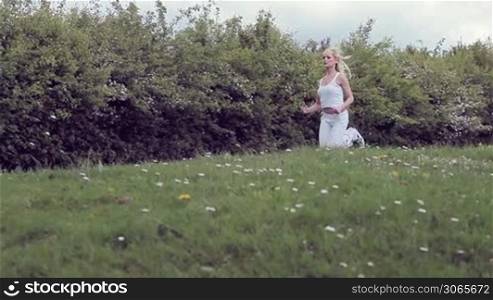 Low angle view of a young blonde woman jogging across a grassy slope in a fitness concept