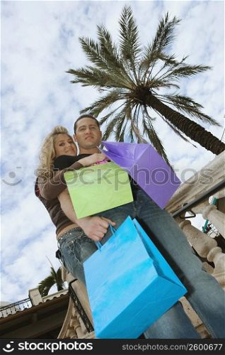 Low angle view of a young couple holding shopping bags and smiling