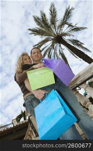 Low angle view of a young couple holding shopping bags and smiling