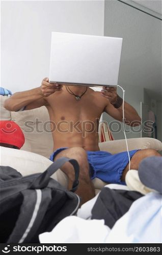 Low angle view of a young man holding a laptop in front of his face