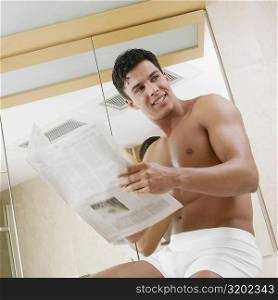 Low angle view of a young man sitting in the bathroom holding a newspaper
