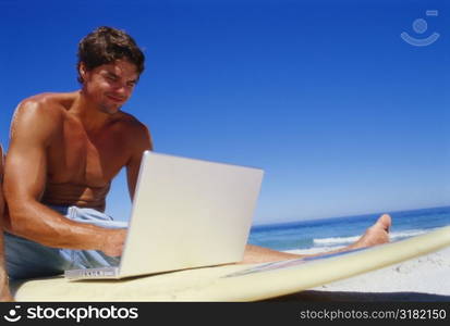 Low angle view of a young man using a laptop on a surfboard