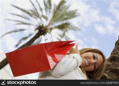 Low angle view of a young woman holding a shopping bag and smiling