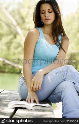 Low angle view of a young woman sitting on a picnic table reading a book