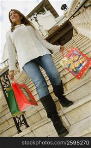 Low angle view of a young woman walking down steps with shopping bags