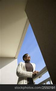 Low angle view of African- American woman standing on balcony smiling leaning on rail looking out.