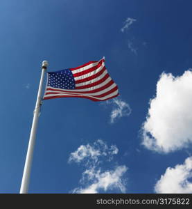 Low angle view of American flag flying with cumulus cloud formation in blue sky.