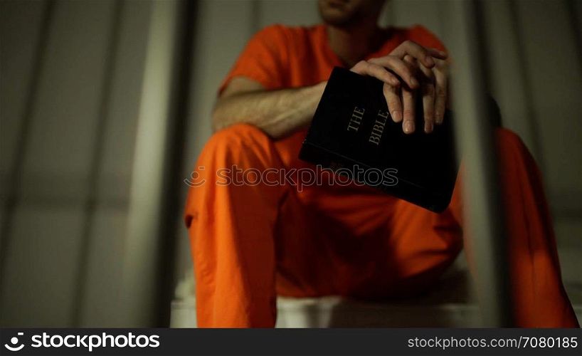 Low angle view of an inmate clutching a bible in prison