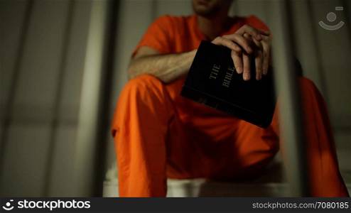Low angle view of an inmate clutching a bible in prison