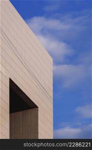 Low angle view of apertures window on gray tile wall of office building against white clouds on blue sky in vertical frame