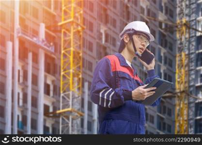 Low angle view of Asian engineer holding computer tablet and talking on smartphone while working in construction site area