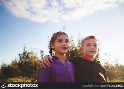 Low angle view of boy outdoors with arms around girl looking away smiling