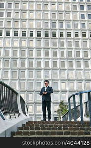 Low angle view of business man standing at top of stairway looking at watch