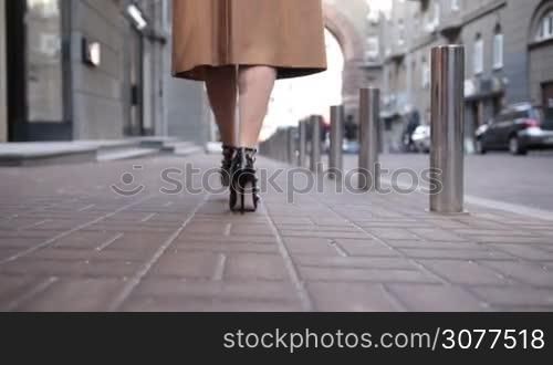 Low angle view of business woman in black high heel shoes walking away in the city street closeup. Rear view of female beautiful legs walking on sidewalk. Slow motion.