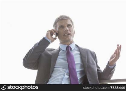 Low angle view of businessman talking on cell phone against sky