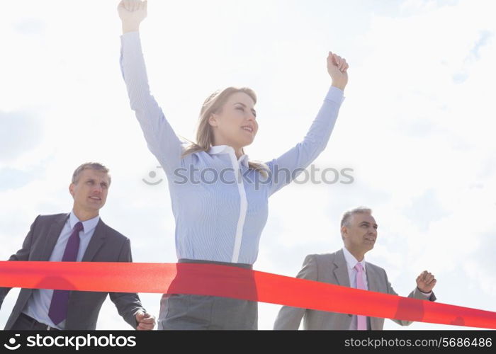 Low angle view of businesswoman crossing finishing line with colleagues in background