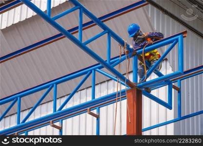 Low angle view of construction worker with safety equipment is welding metal roof warehouse building structure in construction site