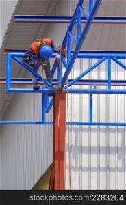 Low angle view of construction worker with safety equipment welding metal roof structure of warehouse building in construction site, work safety concept