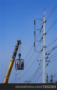 Low angle view of crane truck lifting 2 electricians in metal man basket to working on electric power pole against blue clear sky in vertical frame