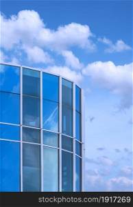 Low angle view of curved glass office building against white clouds on blue sky background in vertical frame