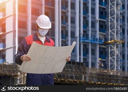 Low angle view of engineer builder in protective face mask looking at project blueprint while working in construction site
