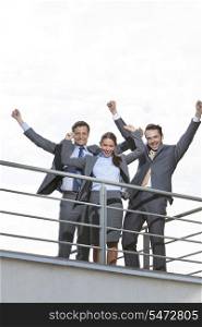Low angle view of excited businesspeople with arms raised on terrace against sky