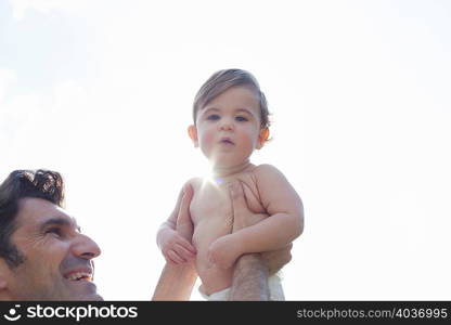 Low angle view of father holding up son, looking at camera