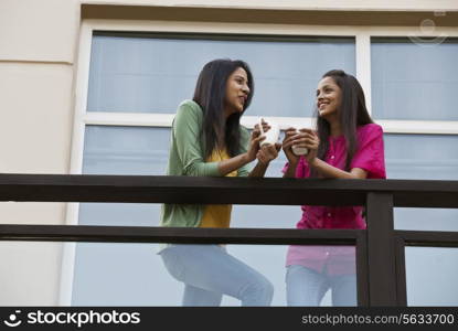 Low angle view of female friends looking at each other while having coffee in balcony