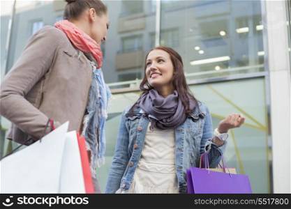 Low angle view of female friends with shopping bags looking at each other against store
