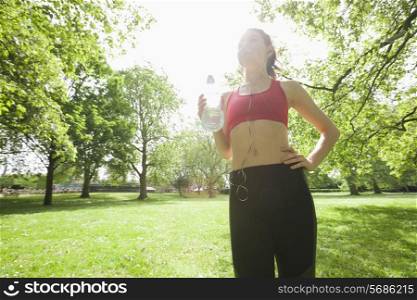 Low angle view of fit woman listening to music while holding water bottle in park