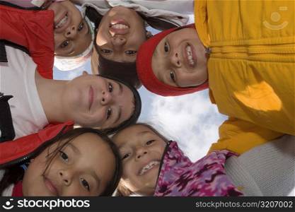 Low angle view of five children and a teenage boy standing in a circle and smiling