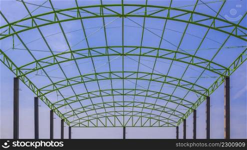 Low angle view of green metal roof structure of industrial building against blue sky in construction site