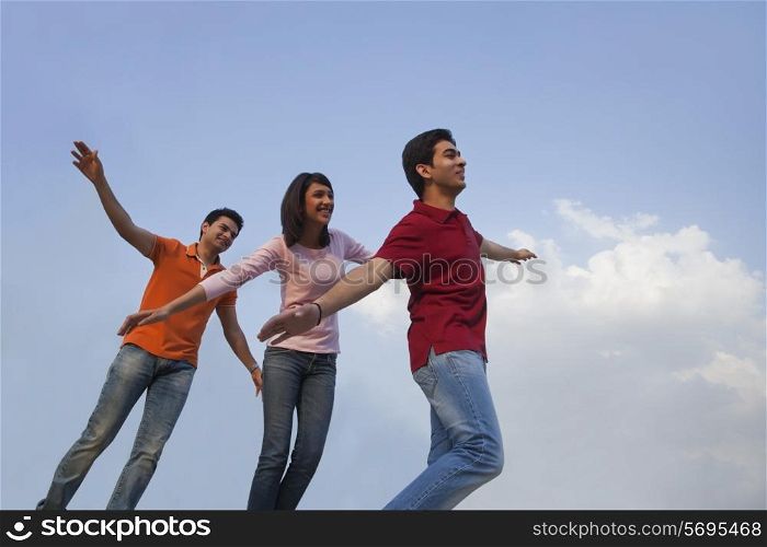 Low angle view of happy friends with arms outstretched against blue sky