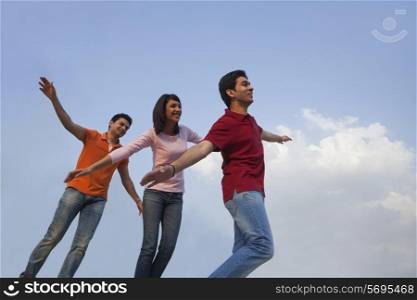 Low angle view of happy friends with arms outstretched against blue sky