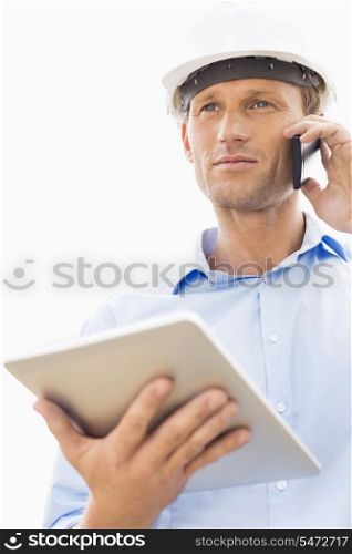 Low angle view of male architect with digital tablet using cell phone against sky