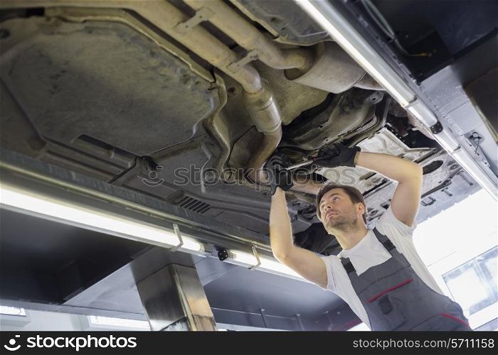 Low angle view of male automobile mechanic repairing car in repair shop