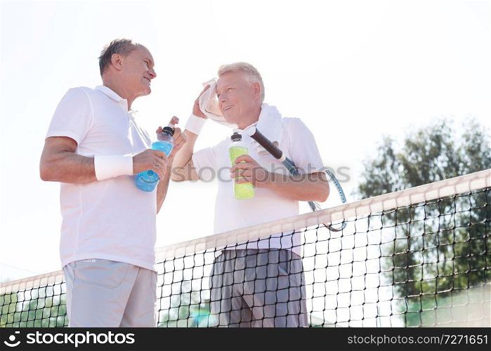 Low angle view of men talking while standing by tennis net against clear sky on sunny day