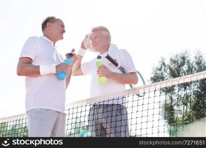 Low angle view of men talking while standing by tennis net against clear sky on sunny day