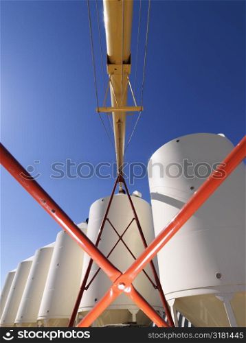 Low angle view of metal grain storage silo facility against blue background.