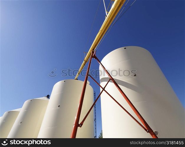 Low angle view of metal grain storage silos against blue background.