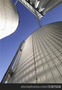Low angle view of metal grain storage silos against blue sky.