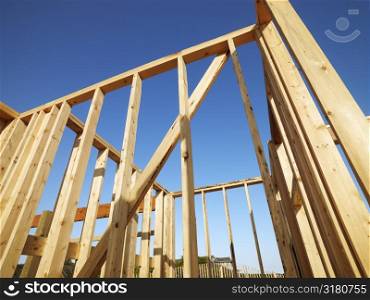 Low angle view of new construction framework for house with blue sky.