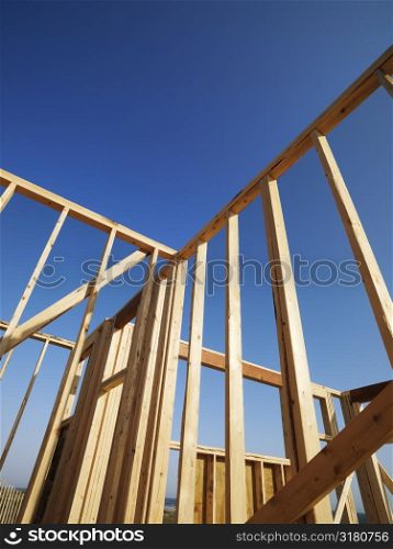 Low angle view of new construction framework for house with blue sky.