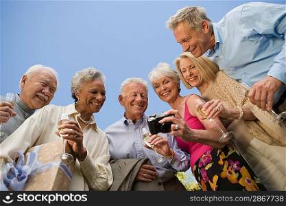 Low angle view of senior woman showing pictures on digital camera to her friends